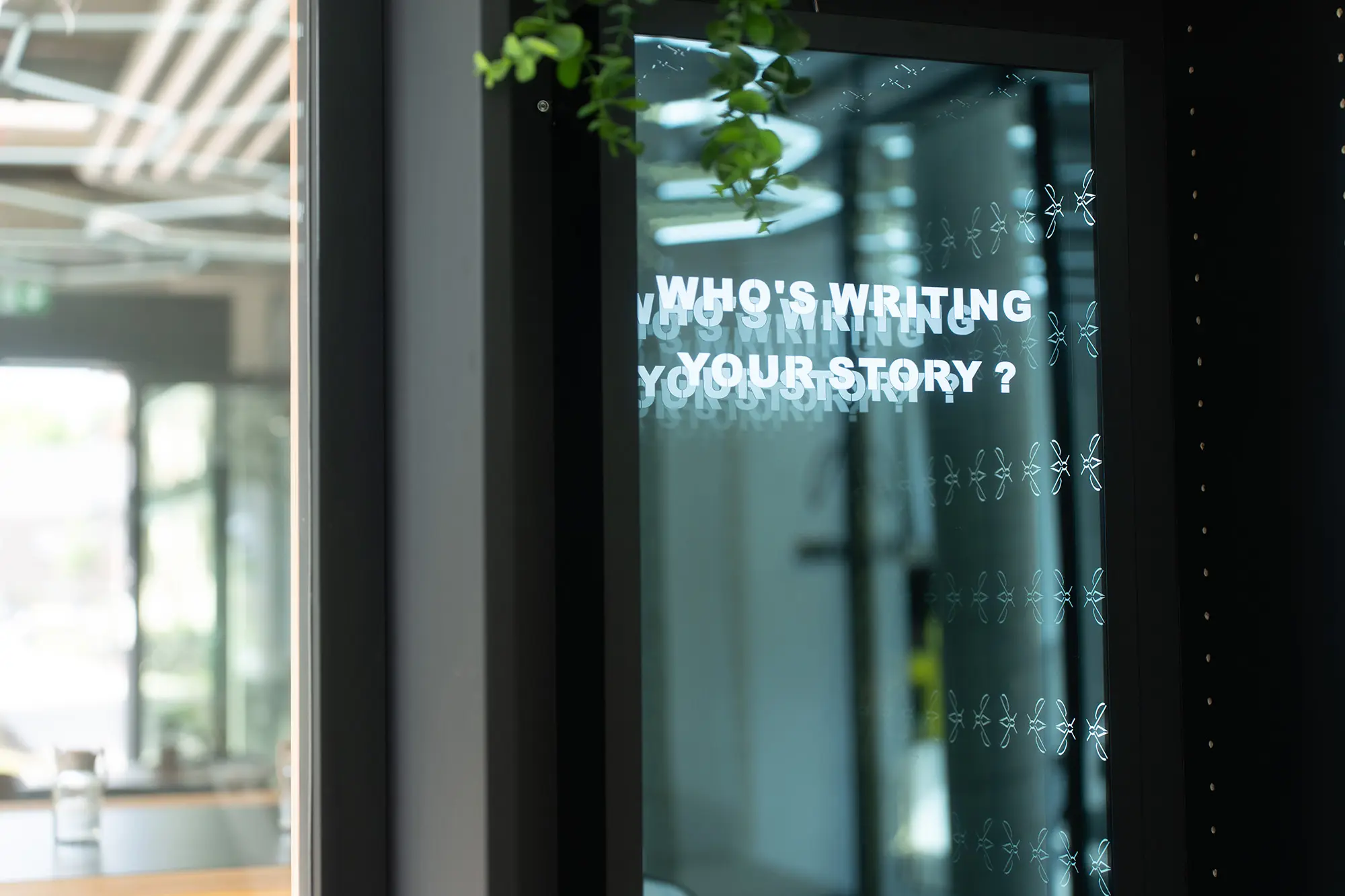 Auf einer Spiegelfläche steht in weißen Buchstaben die Frage Who is writing your story. Auf dem Glas wiederholt sich das Mückenzeichen als feines Muster.